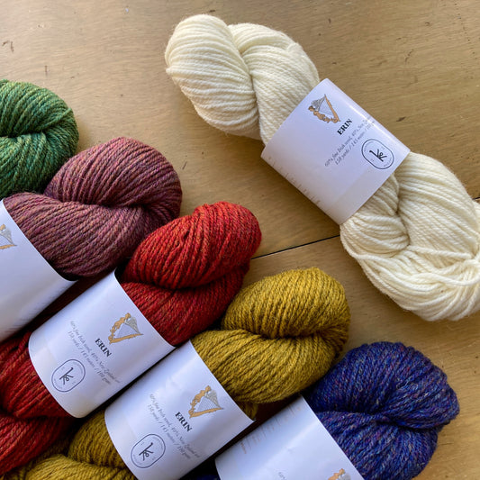 Colorful skeins of Kelbourne Woolens Erin yarn arranged on a wooden surface. 