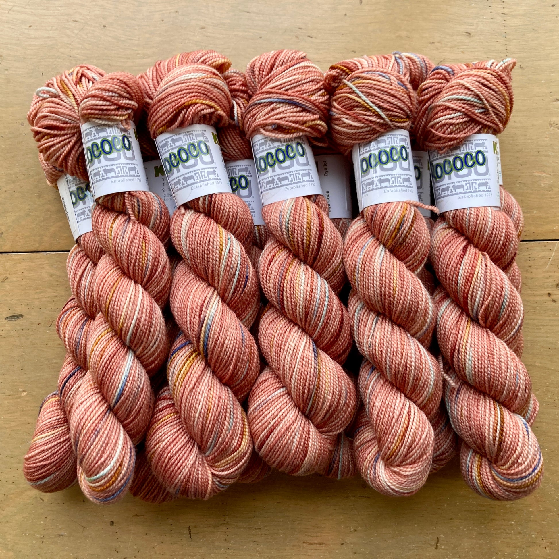 Coral and pink variegated skeins of Koigu KPPPM yarn arranged on a wooden surface. 