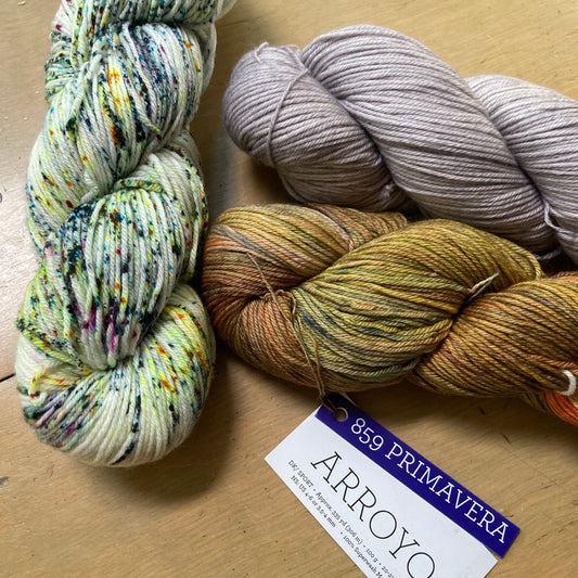 Three colorful skeins of Malabrigo Arroyo yarn arranged on a wooden surface. 