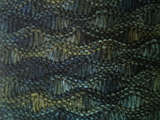 Close up on a handknit drop stitch scarf in shades of dark green and yellow. 