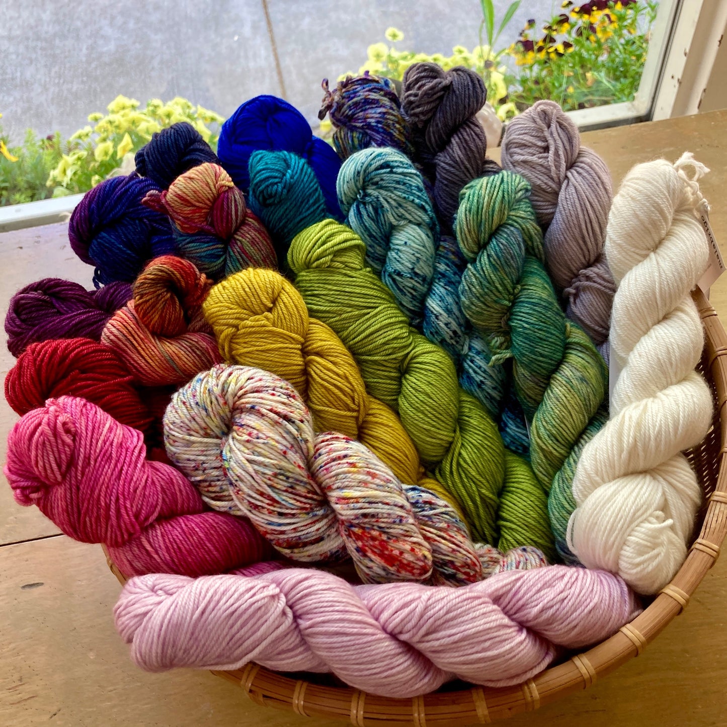 Colorful skeins of Malabrigo Caprino yarn in a basket on a table in front of a window. 