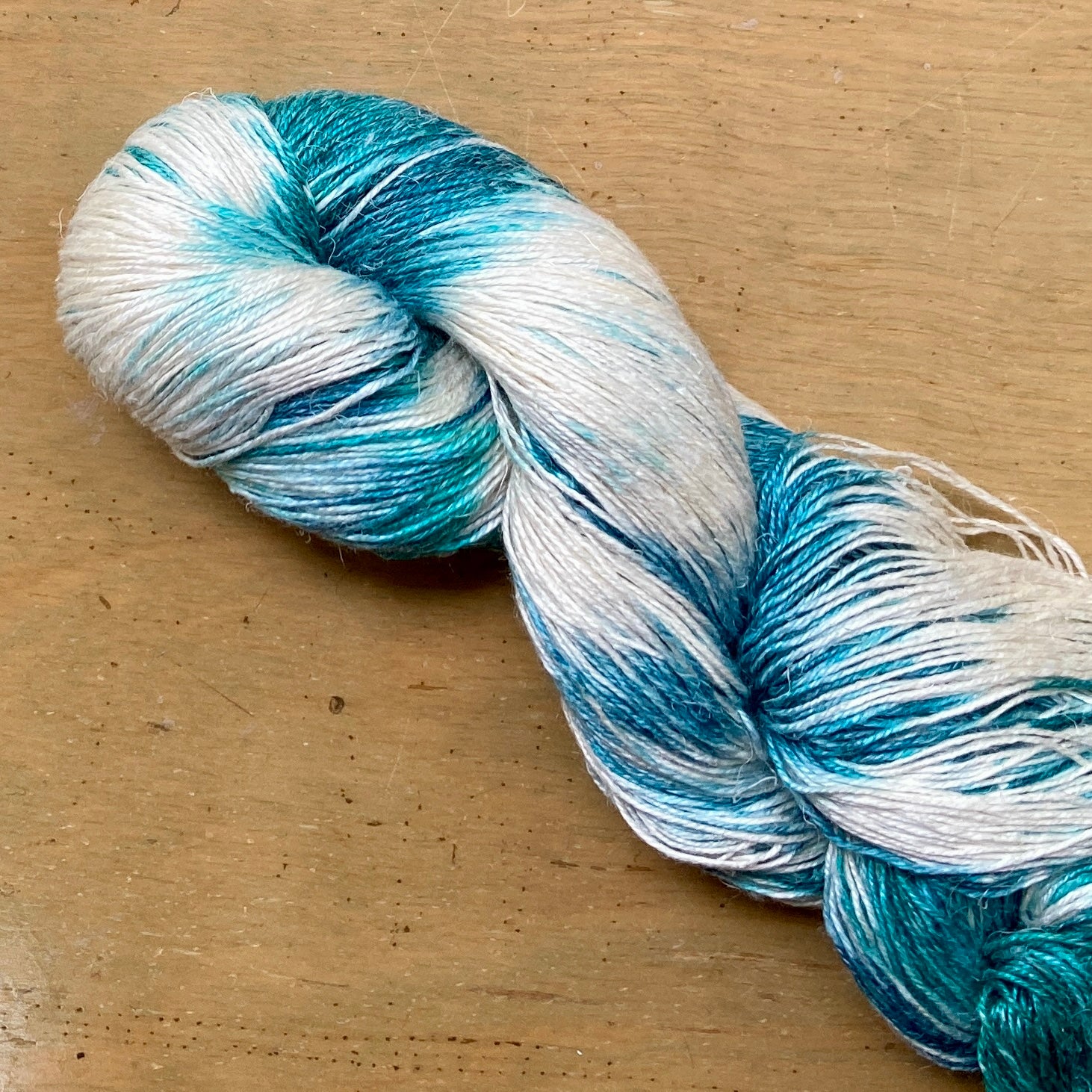 Close up on a variegated white and teal skein of Hand Maiden Flyss yarn, Maldives colorway