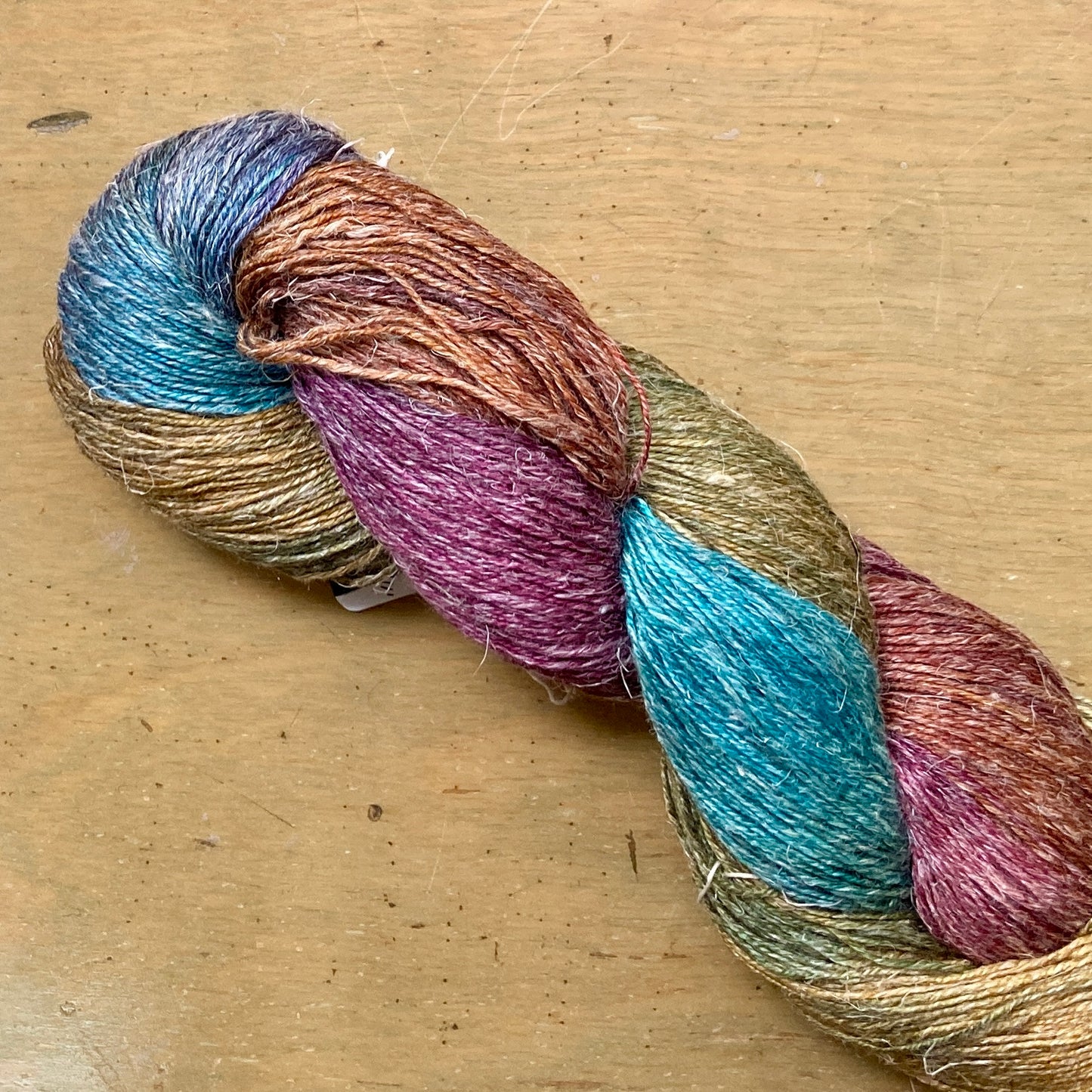 Close up on a variegated burgundy, teal, and brown skein of Hand Maiden Flyss yarn, Paris colorway