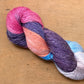 Close up on a variegated pink, eggplant, blue, and orange skein of Hand Maiden Flyss yarn, Santorini colorway