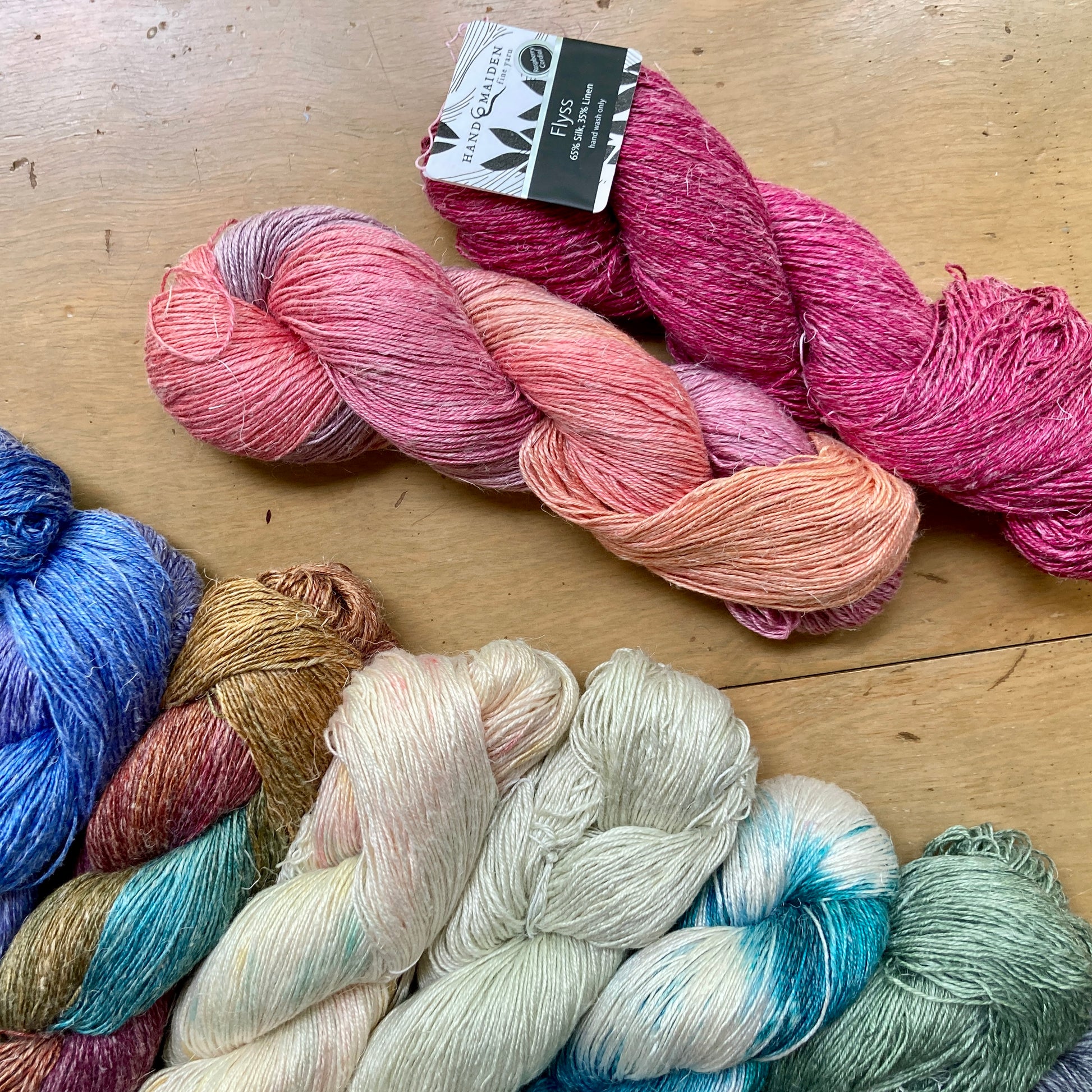 Colorful skeins of Hand Maiden Flyss yarn on a wooden surface, for sale at Hillsborough Yarn Shop, NC, USA.