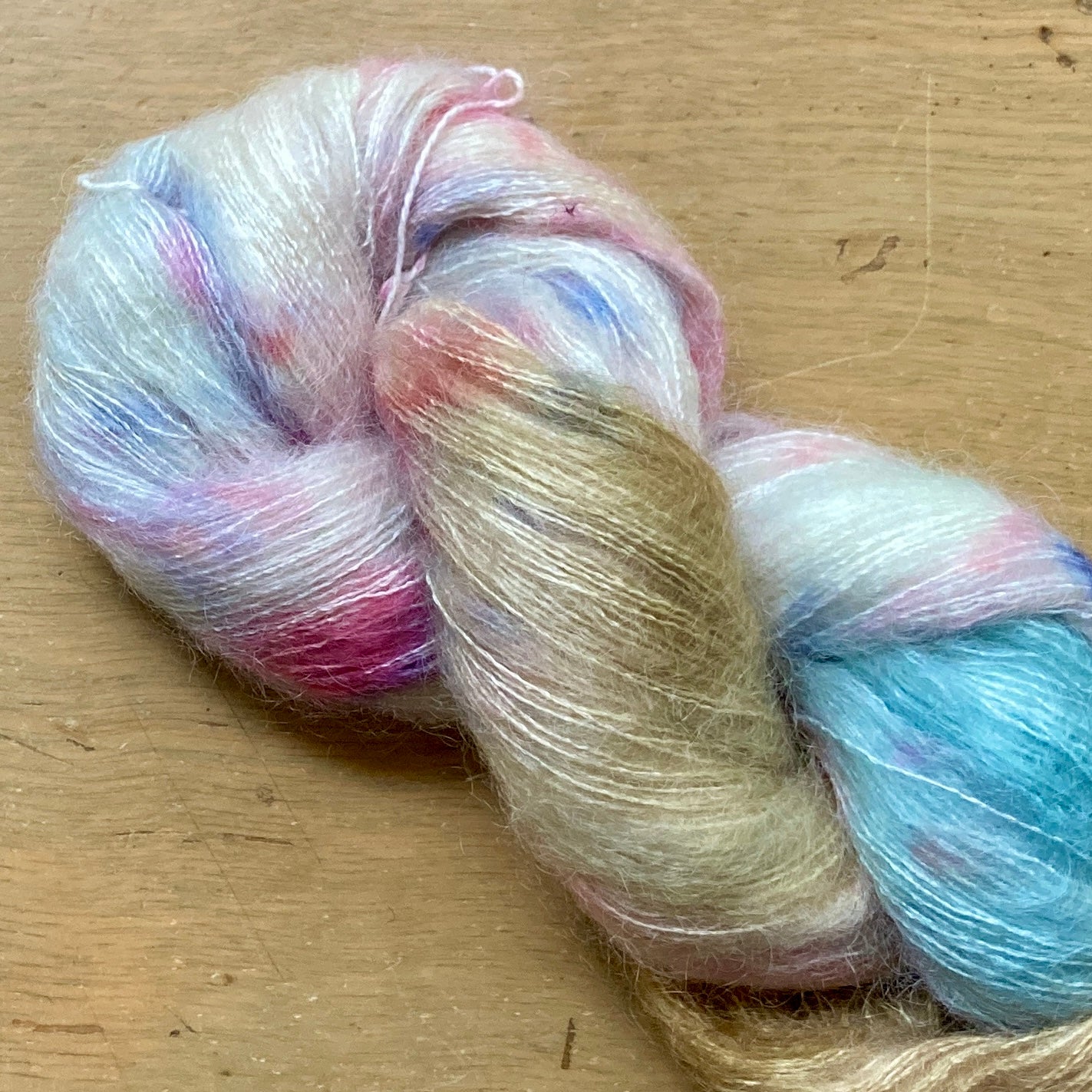 Variegated cream, blue, pink and gold skein of Hand Maiden Superkid Silk yarn. 