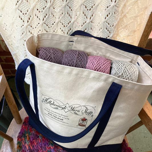 Hillsborough Yarn Shop tote bag filled with pink and purple yarn.