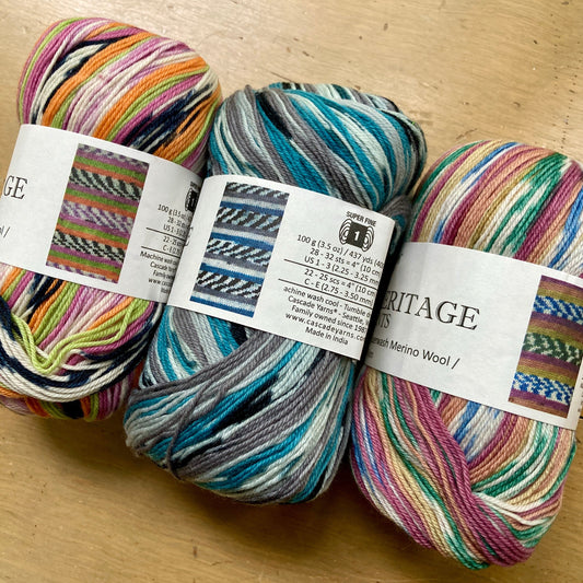 3 colorful balls of Cascade Heritage Prints self patterning yarn on a wooden surface.