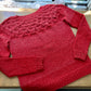 Handknit textured red sweater, lying on a wooden table with a ballwinder attached. 