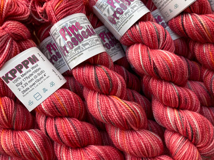 Coral pink variegated skeins of Koigu KPPPM yarn arranged on a wooden surface. 