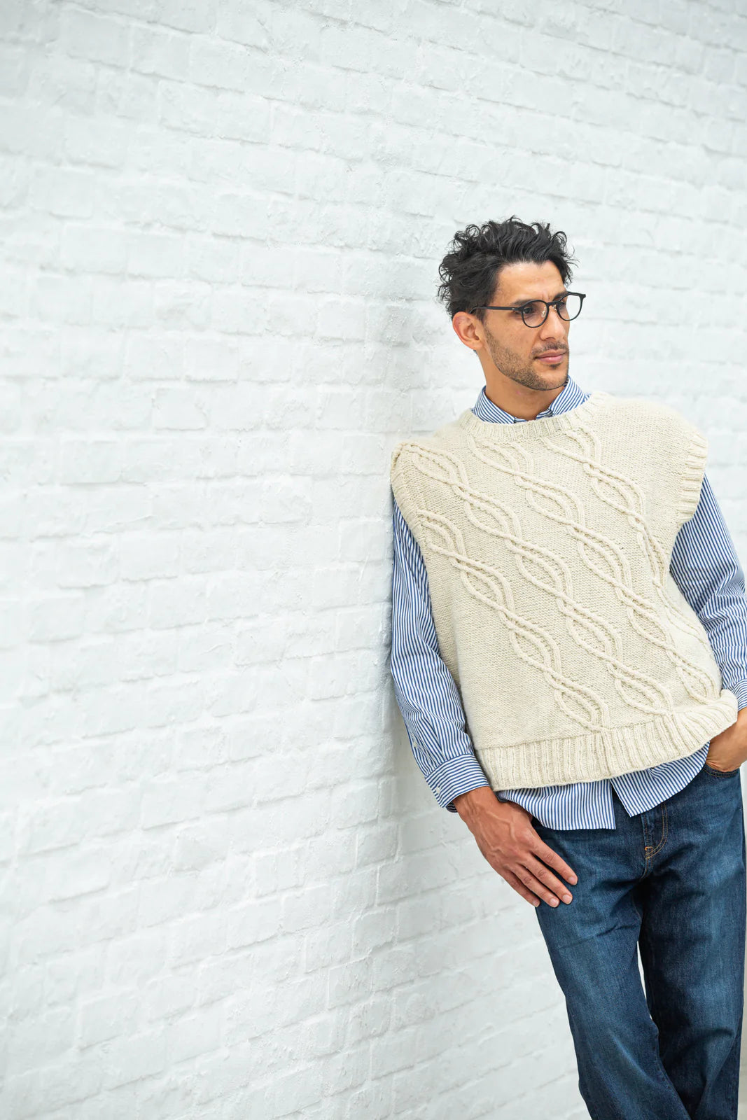 Person wearing white handknit sweater stands before brick wall, showing off a pattern from Brooklyn Tweed’s Northern Lights book. 