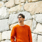 Person wearing orange handknit sweater stands before rock wall, showing off a pattern from Brooklyn Tweed’s Northern Lights book. 