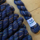 Indigo variegated skeins of Koigu KPPPM yarn arranged on a wooden surface. 