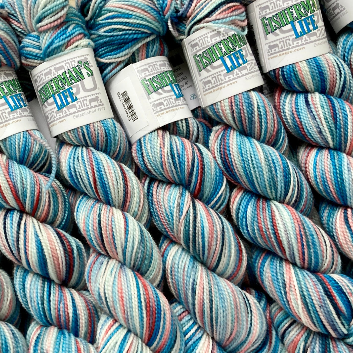 Ocean blue, pale aqua, and salmony pink/red variegated skeins of Koigu KPPPM yarn. 