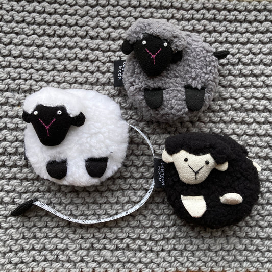 Three sheep-shaped tape measures lying on a handknit gray blanket. 