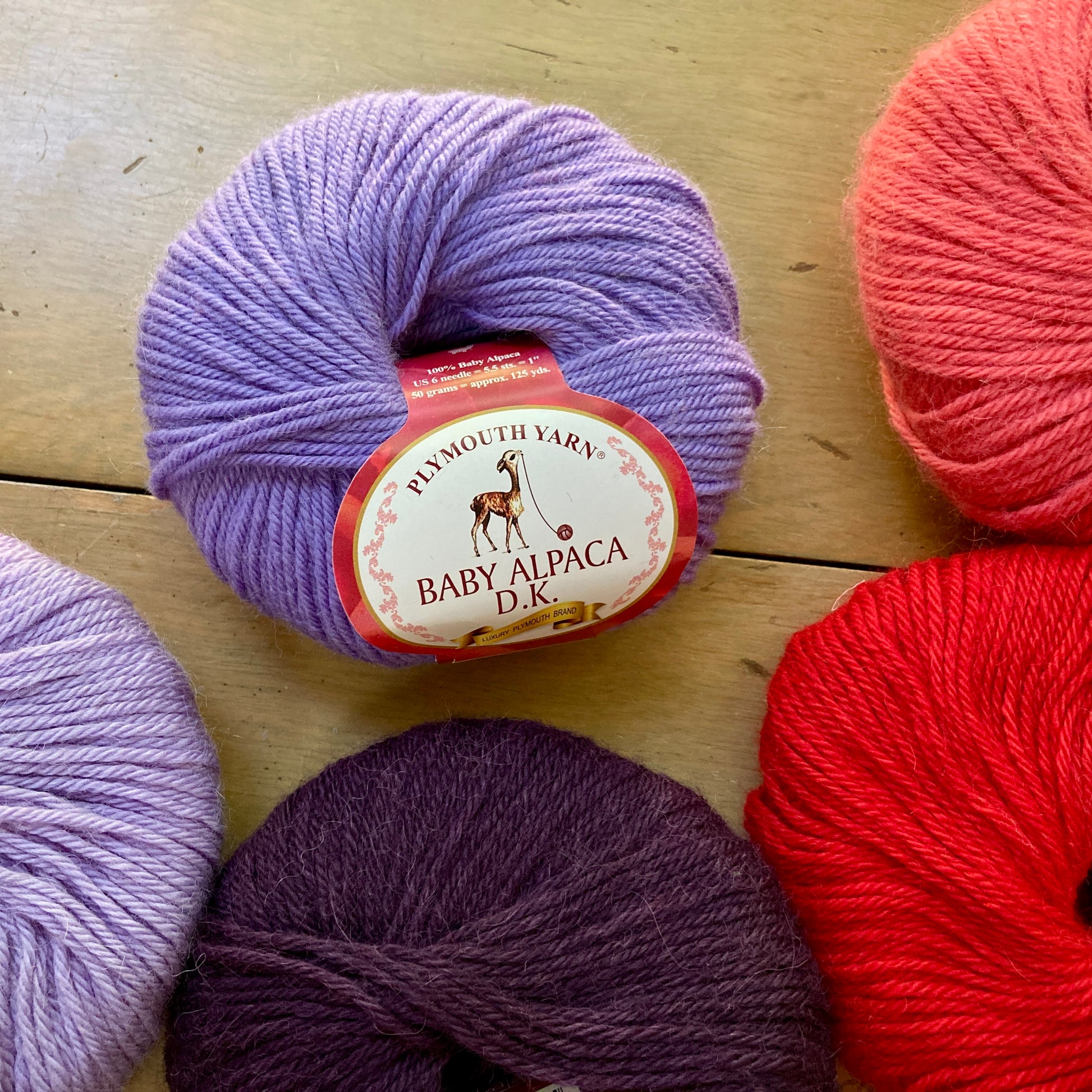 Purple, pink, and red balls of Plymouth Baby Alpaca DK yarn. 