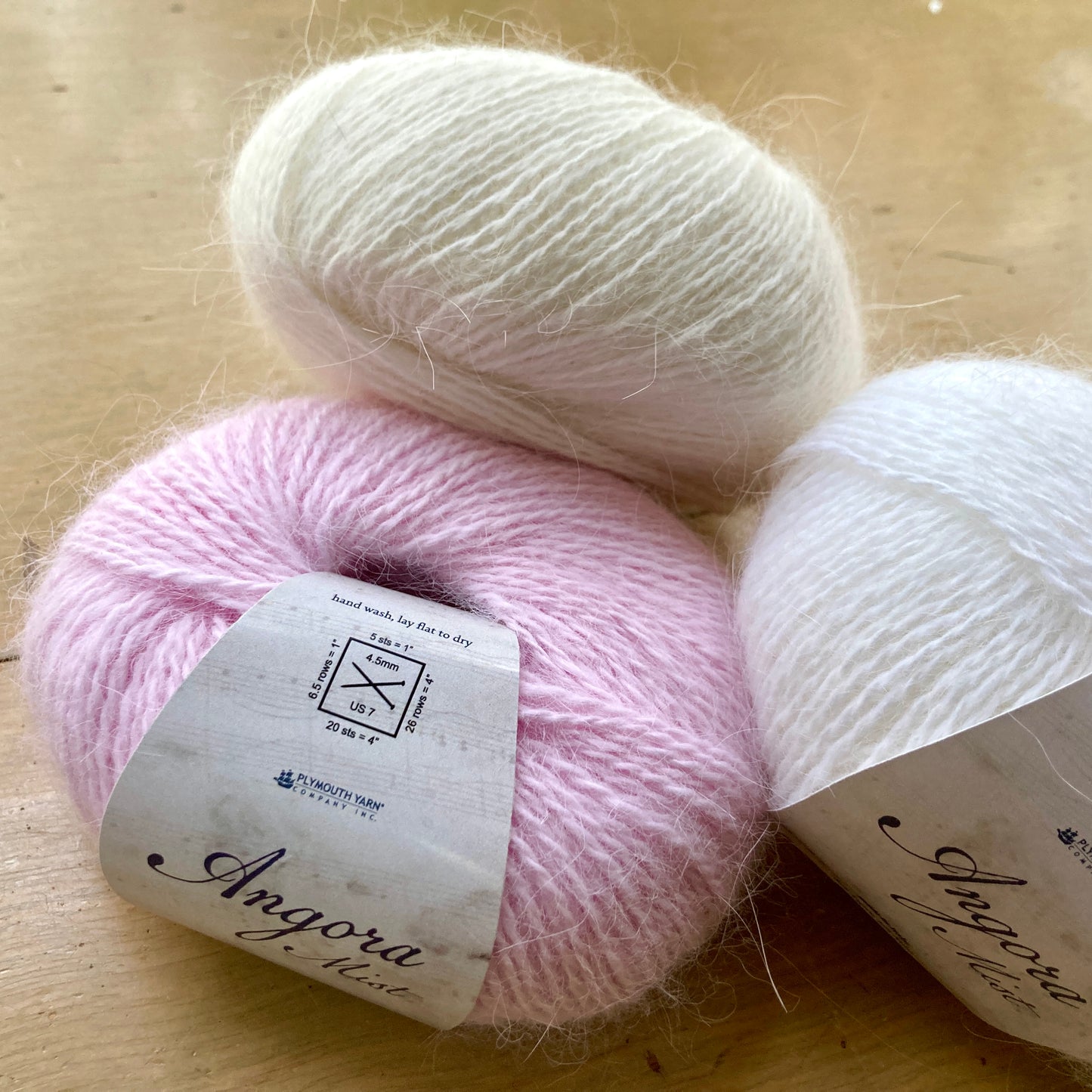 Three balls of Plymouth Yarn Angora Mist in baby pink, cream, and white