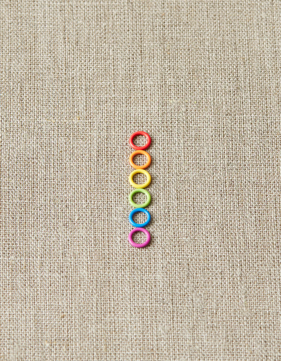 Colorful ring stitch markers on a light gray background. 