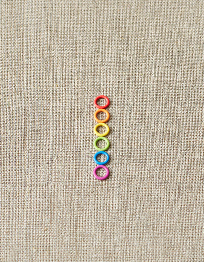 Colorful ring stitch markers on a light gray background. 
