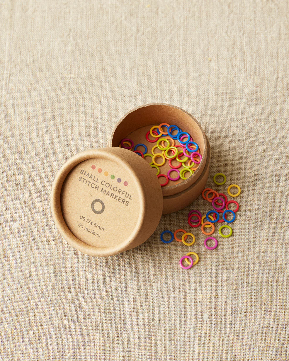 Open box of colorful cocoknits stitch markers on a light gray surface.  