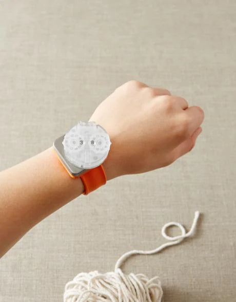 Close up on a white hand wearing an orange magnetic slap bracelet with a white row counter attached, like a watch. 