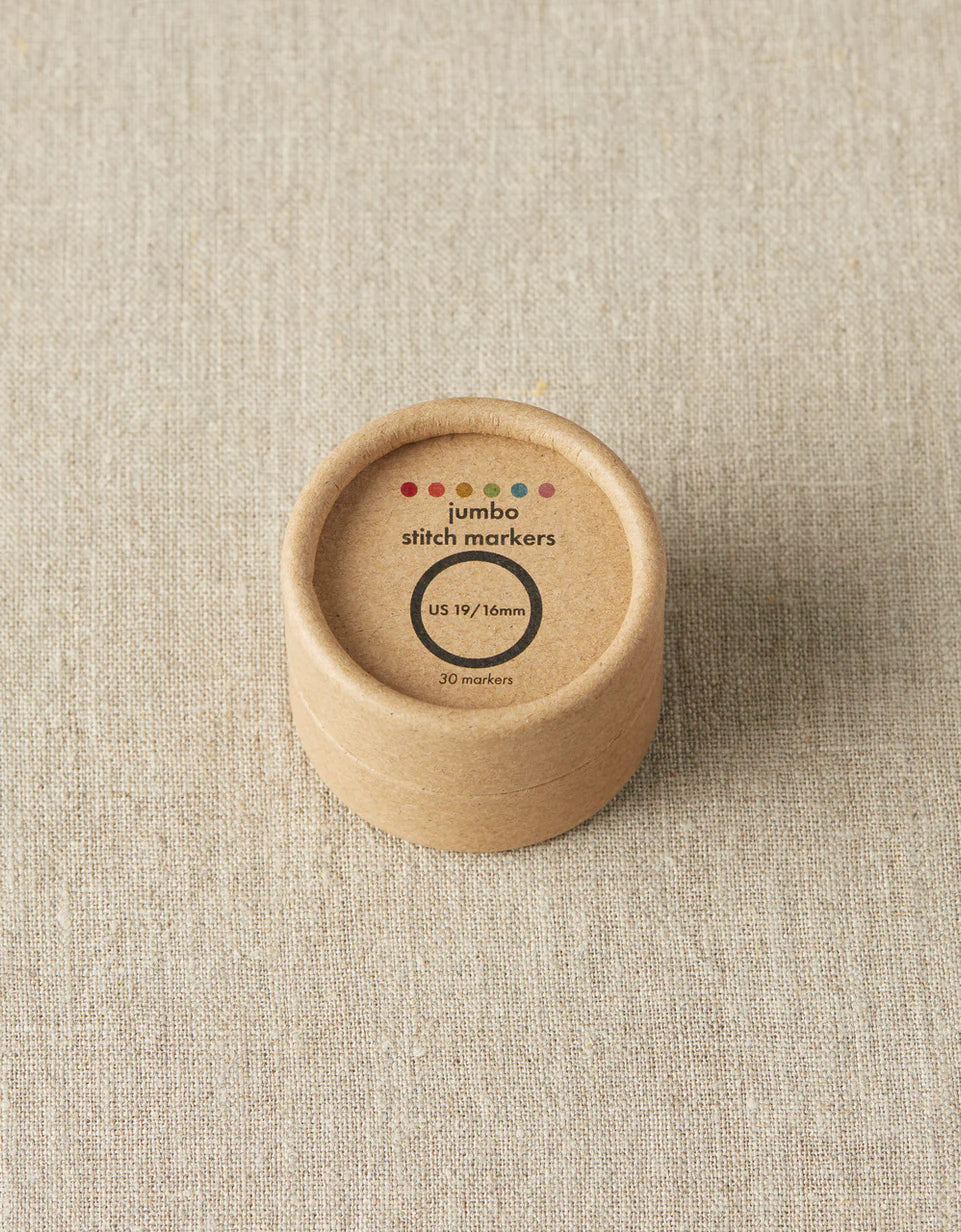 Kraft brown box of cocoknits Jumbo Stitch Markers on a gray surface. 
