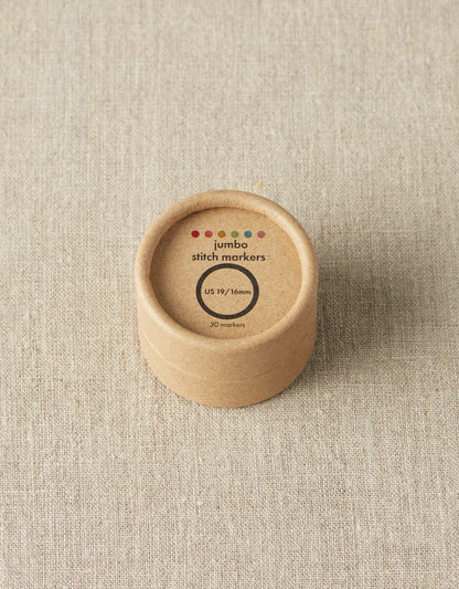 Kraft brown box of cocoknits Jumbo Stitch Markers on a gray surface. 