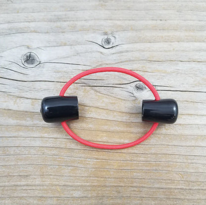 Double point knitting needle holder with two black plastic endcaps, connected by red elastic. 