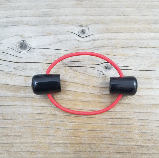 Double point knitting needle holder with two black plastic endcaps, connected by red elastic. 