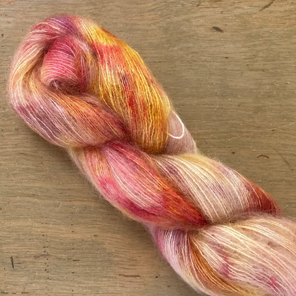 Speckled red, peach, and gold skein of Fleece Artist / Hand Maiden Superkid Silk yarn, colorway Honeycomb