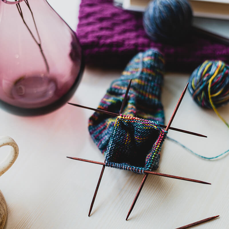 Handknit sock in progress, shown in turquoise variegated yarn on a set of 5 brown cubics double pointed needles. 