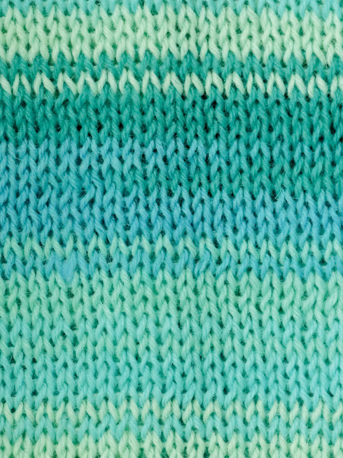 Close-up of a knitted fabric with horizontal striped gradient effect in green and blue.